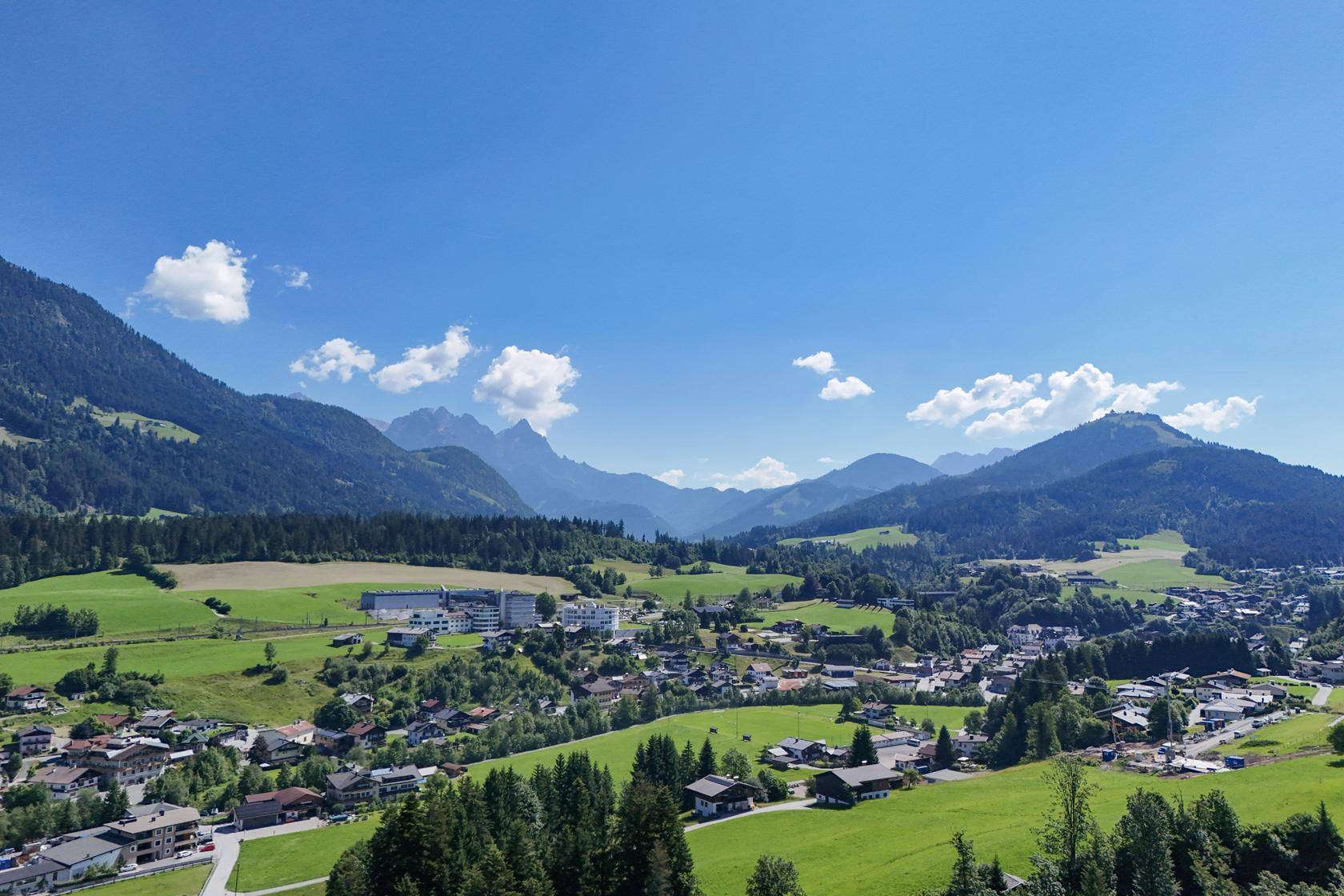 Malerischer Panoramablick über ein alpines Tal mit grünen Wiesen und Bergen.