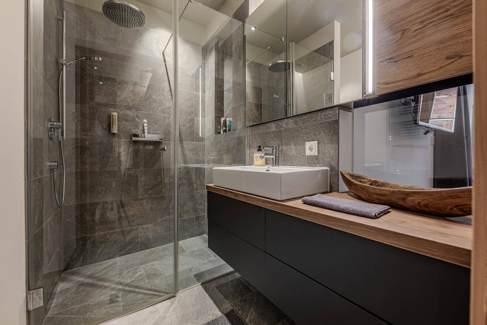 Modernes Badezimmer mit großer begehbarer Dusche, Einzelwaschbecken und grauen Fliesen.