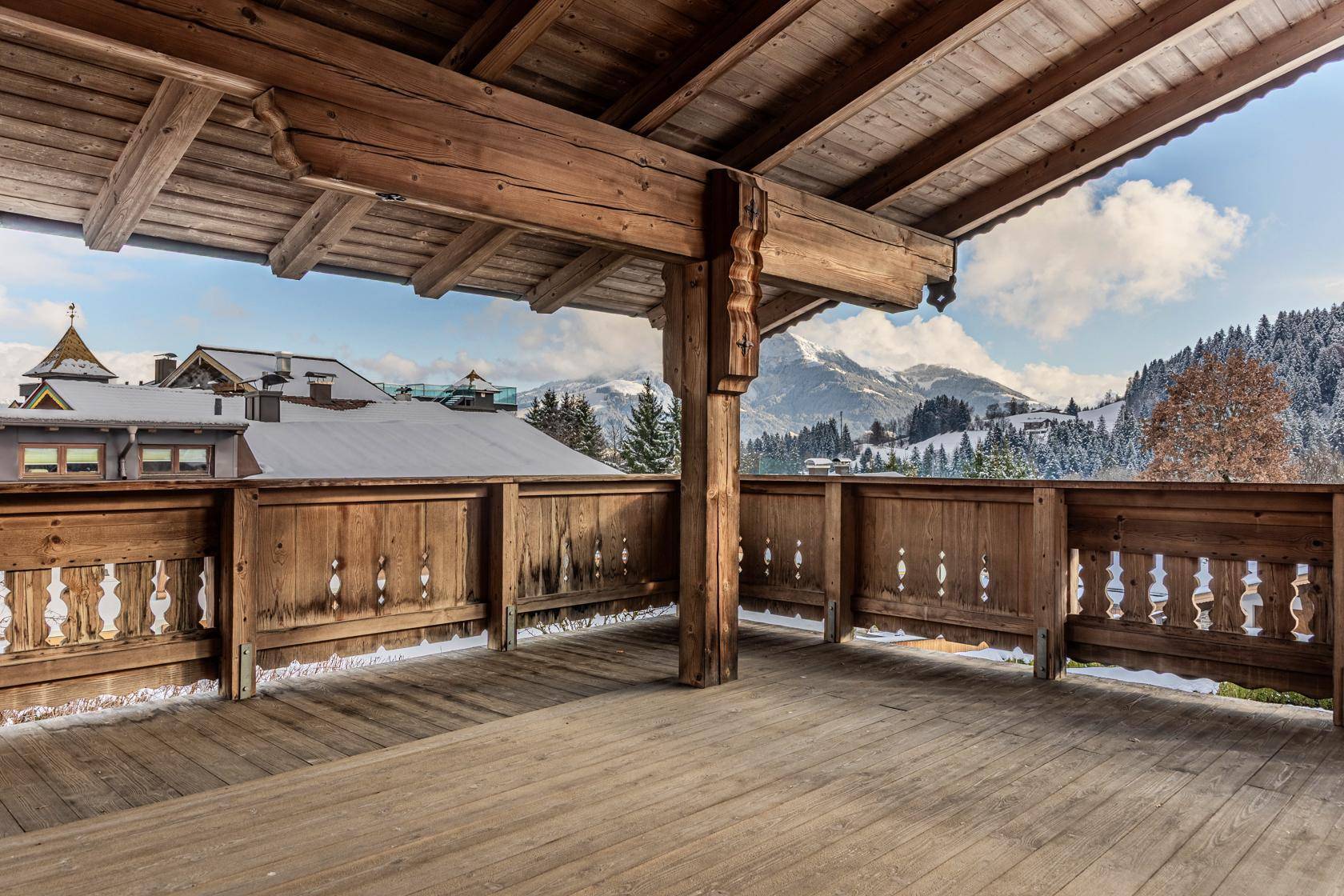 Geräumiger Holzbalkon mit traditionellem Geländer und malerischem Blick auf die verschneiten Berge.