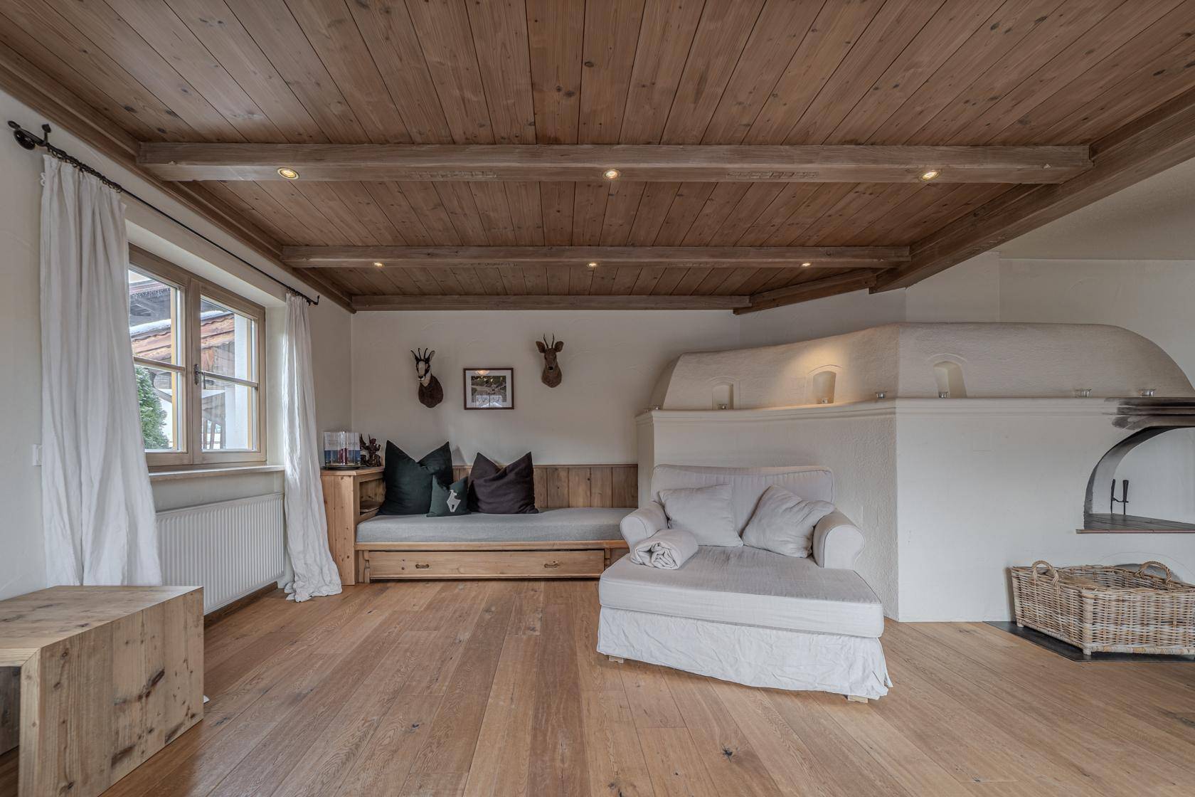 Gemütliches Wohnzimmer mit Holzbalkendecke, hellem Holzboden und traditionellem Kachelofen.