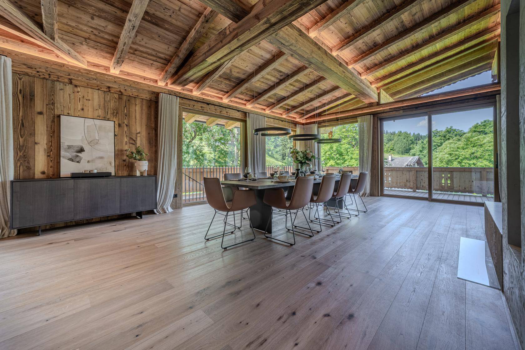 Heller Essbereich mit Holzbalkendecke, großem Esstisch und Zugang zum Balkon mit Bergblick.