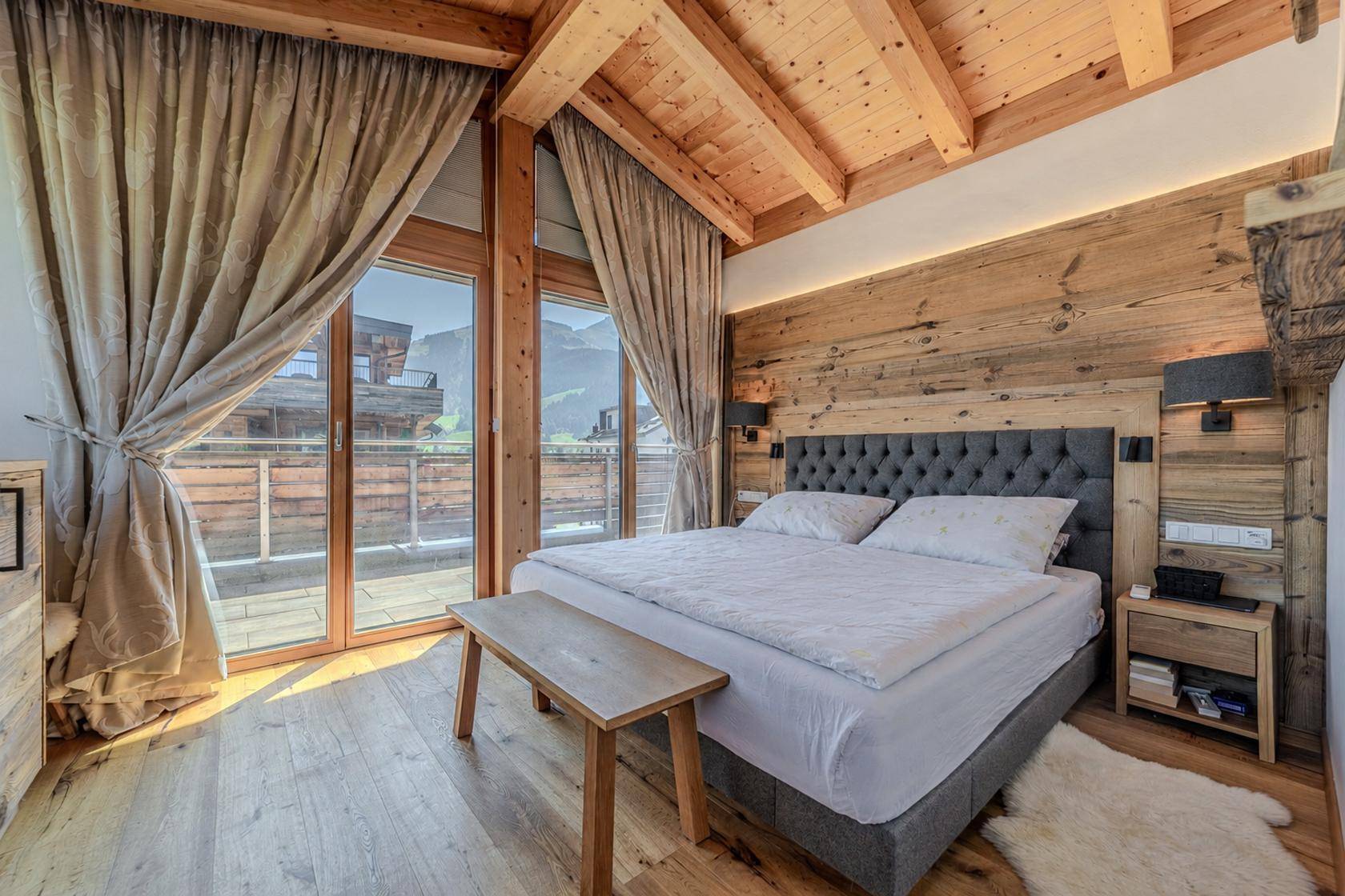 Gemütliches Schlafzimmer mit Holzwänden, Holzbalkendecke und Balkonzugang.