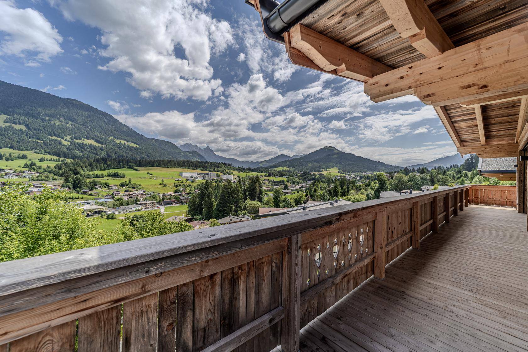 Langer Holzbalkon mit geschnitztem Geländer und atemberaubendem Panoramablick auf die Alpen.