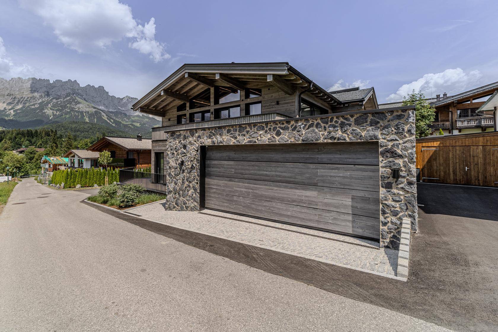 Moderne Villa mit Steinfassade und integrierter Garage in alpiner Umgebung mit Bergblick.