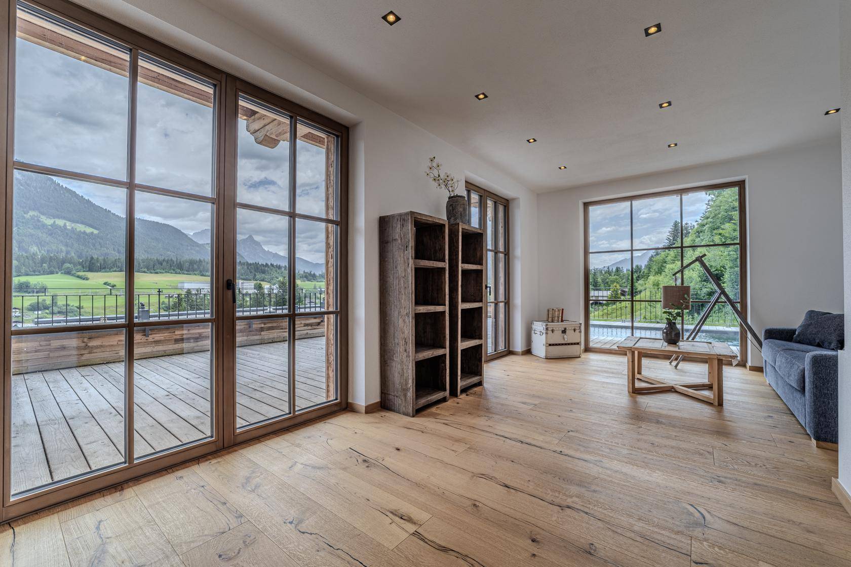 Heller Wohnraum mit Holzboden, großen Fenstern und Zugang zu einem Balkon mit Bergblick.
