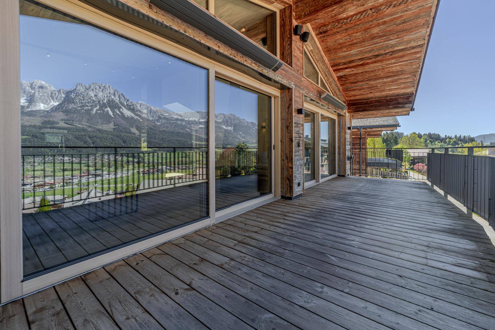 Großer Holzbalkon mit raumhohen Fenstern und weitem Blick auf die Alpen.