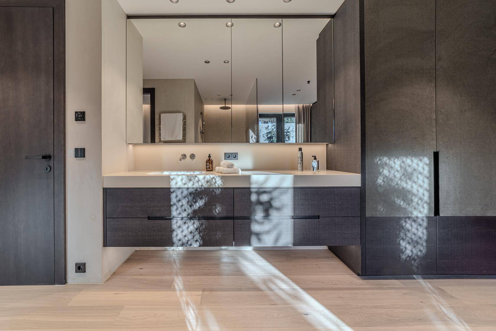 Modernes Badezimmer mit schwebendem Waschtisch, großem Spiegelschrank und dunklen Holzfronten.