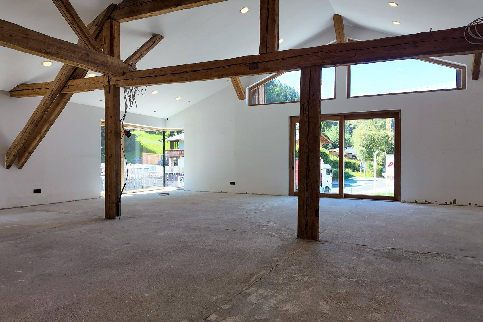Heller, offener Wohnbereich mit hohen Decken, sichtbaren Holzbalken und großen Fenstern mit Blick ins Grüne.