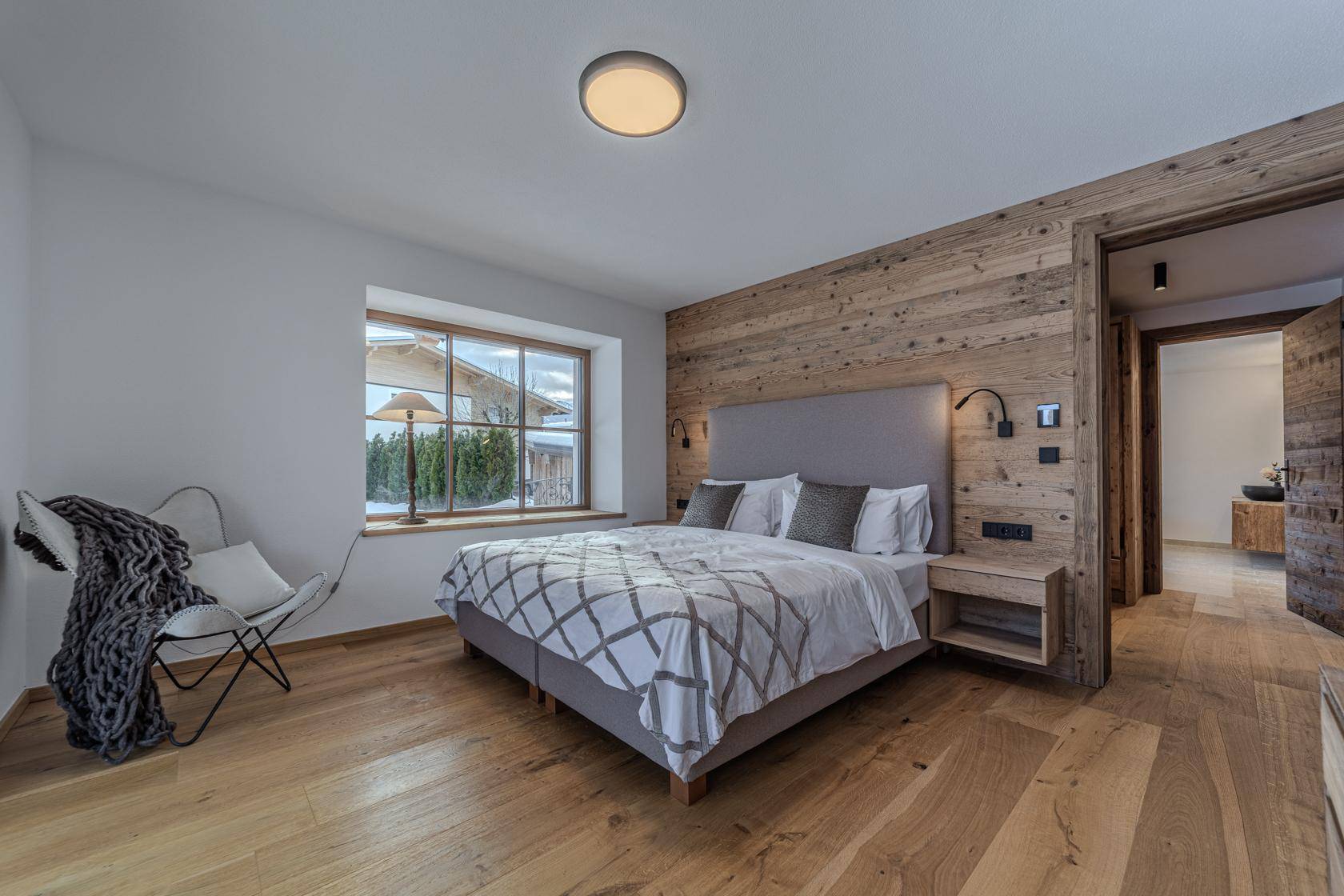 Gemütliches Schlafzimmer mit Holzwand, Holzboden und Fenster mit Blick ins Grüne.