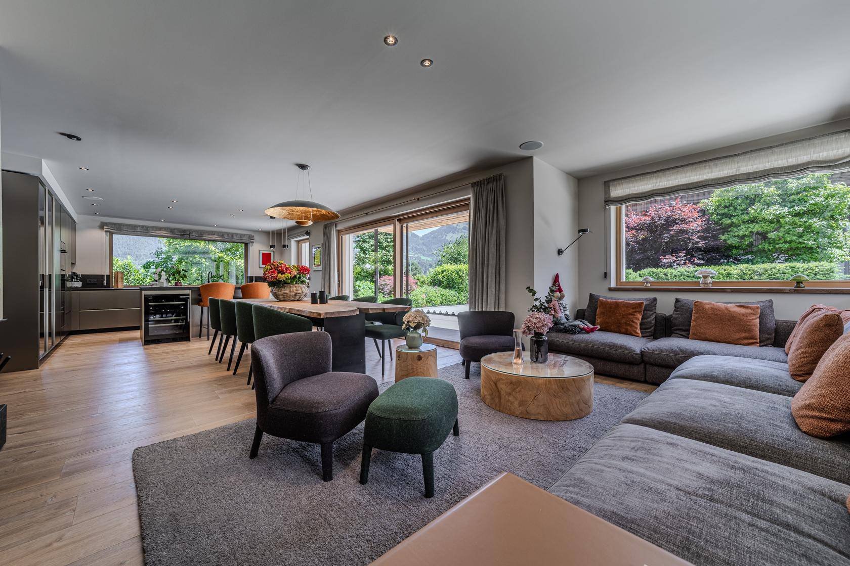 Heller offener Wohn-Essbereich mit großzügigem Sofa, Holzboden und großen Fenstern mit Bergblick.