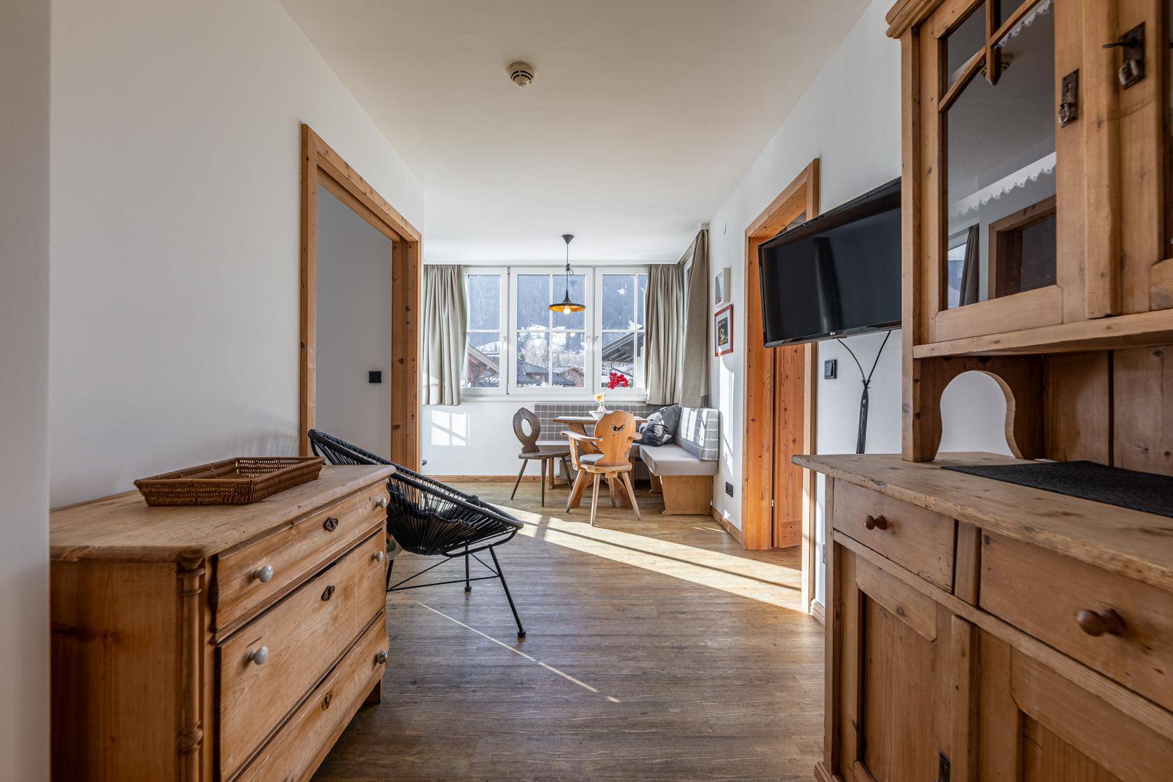 Gemütlicher Wohnbereich mit traditionellen Holzmöbeln, Wandfernseher und Blick auf die Berge.