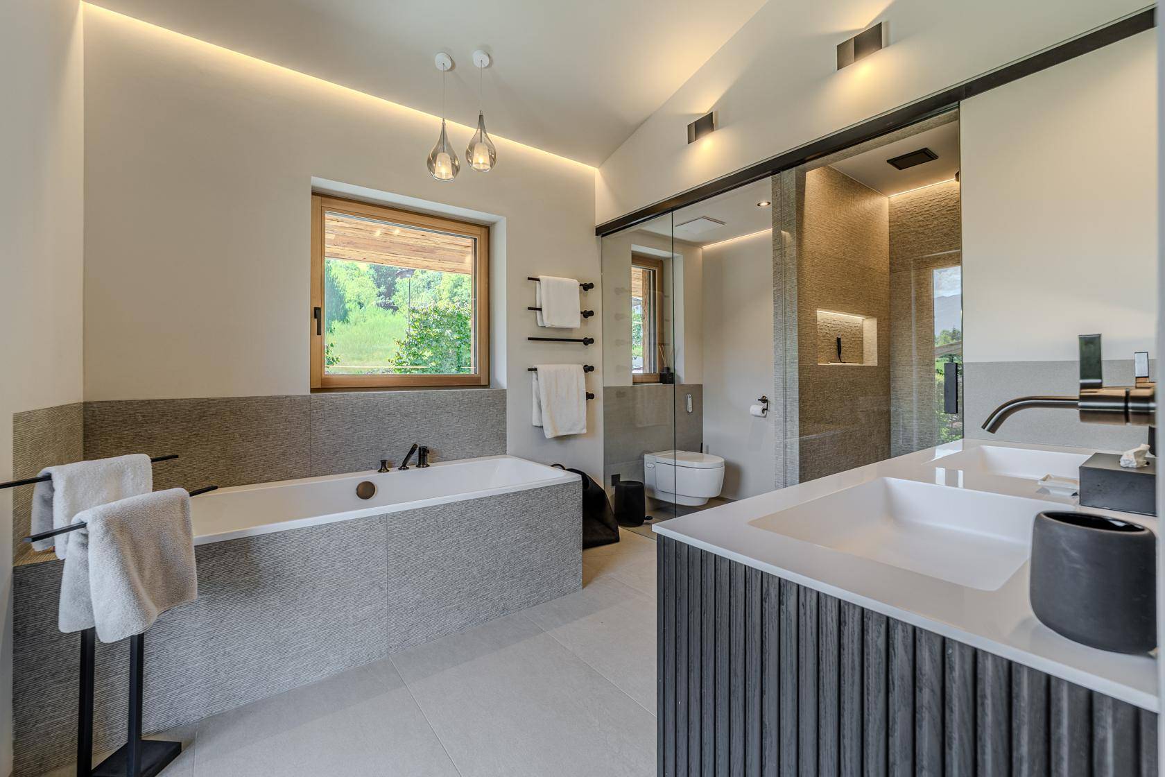 Modernes Badezimmer mit Badewanne, begehbarer Dusche, Doppelwaschbecken und Fenster mit Bergblick.