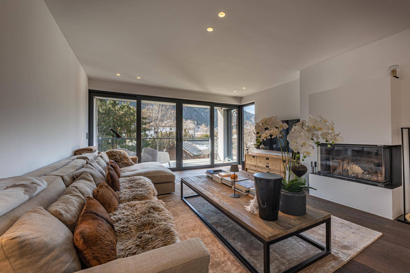 Gemütliches Wohnzimmer mit Kamin, großzügigen Fenstern und Bergblick.