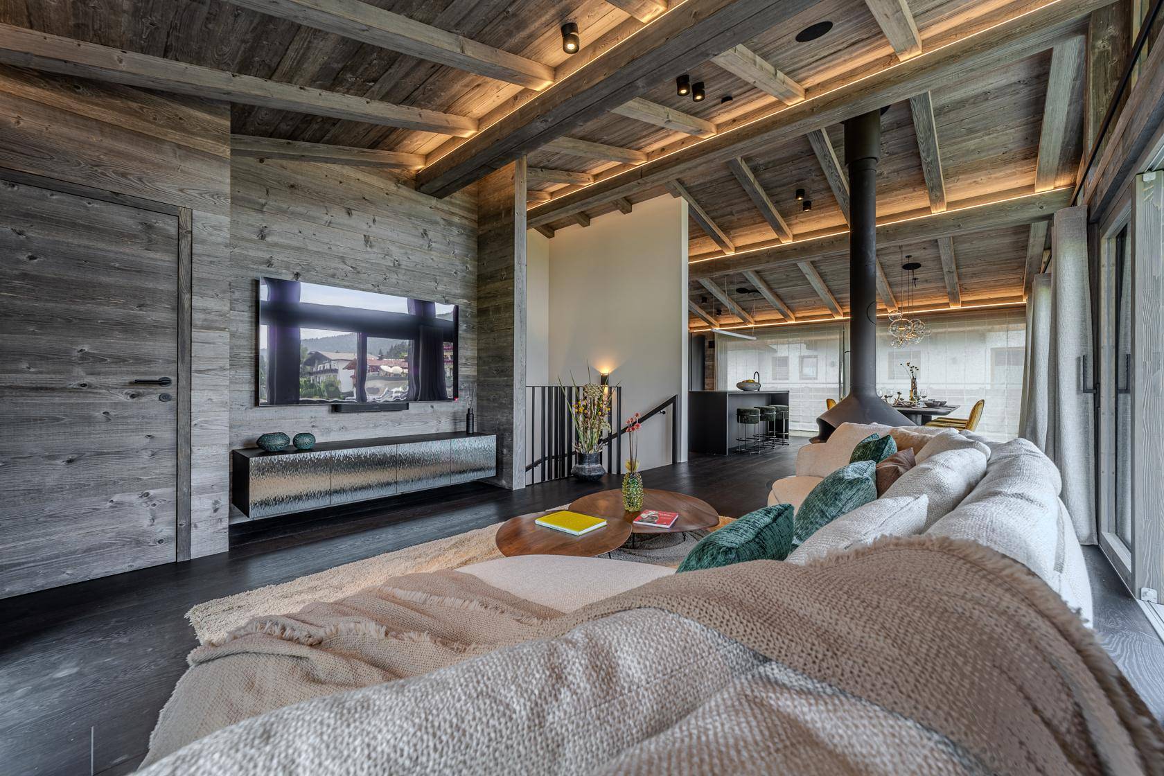 Geräumiger Wohnbereich mit bequemer Couch, Wandfernseher und Blick auf den offenen Essbereich.