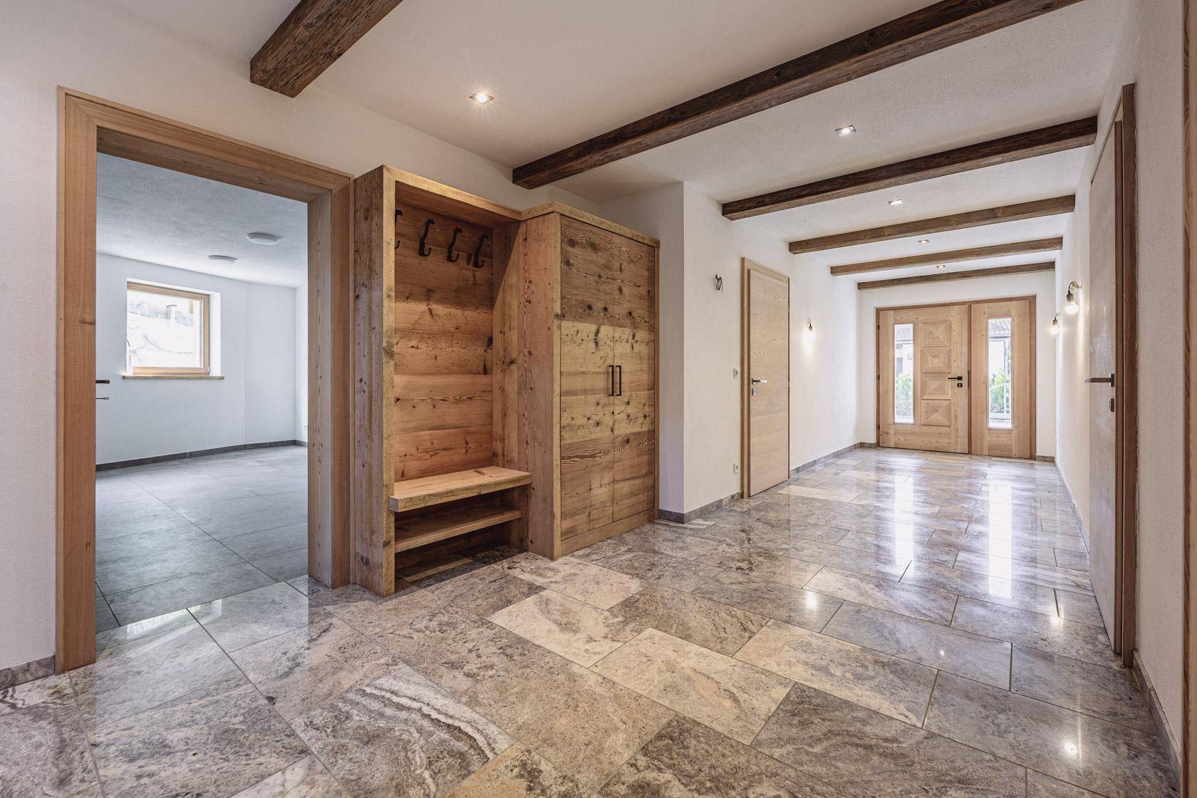Geräumiger Eingangsbereich mit Natursteinboden, Holzbalken und Garderobe.