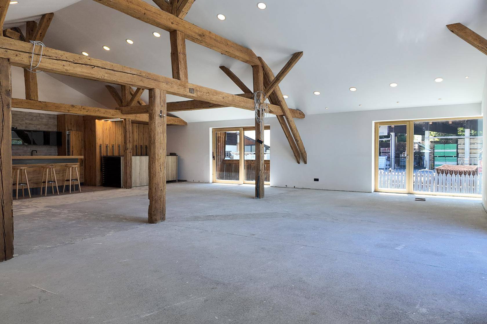 Weitläufiger Wohnbereich mit hohen Decken, Holzbalken und großen Schiebetüren, die nach draußen führen.