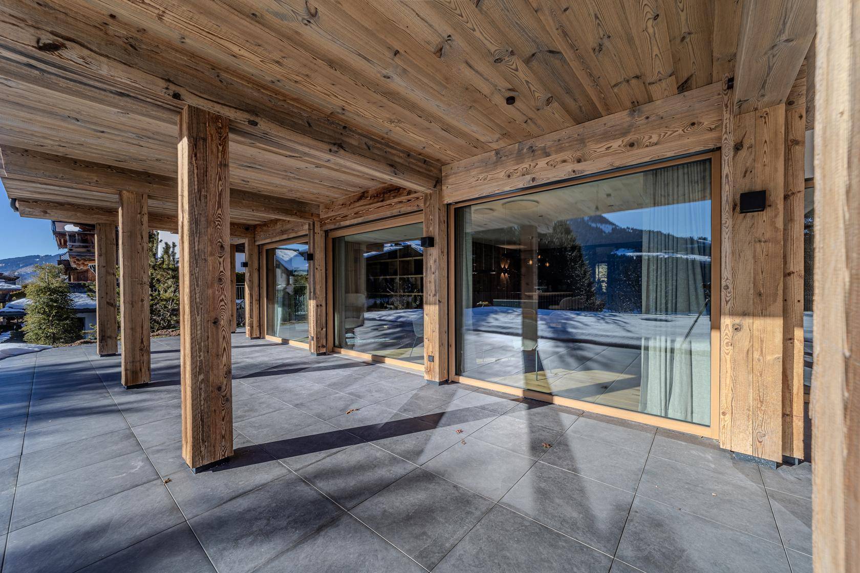 Überdachte Terrasse mit Holzelementen und Zugang zu den Innenräumen mit Bergblick.