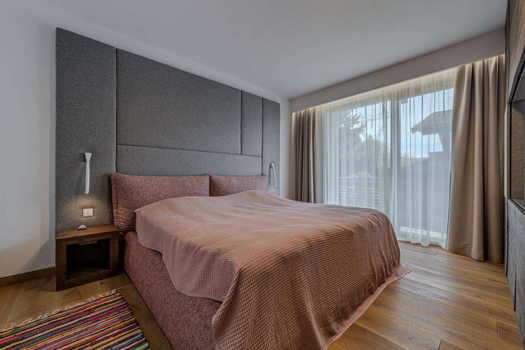 Helles Schlafzimmer mit großem Fenster, gepolstertem Kopfteil und Holzboden.