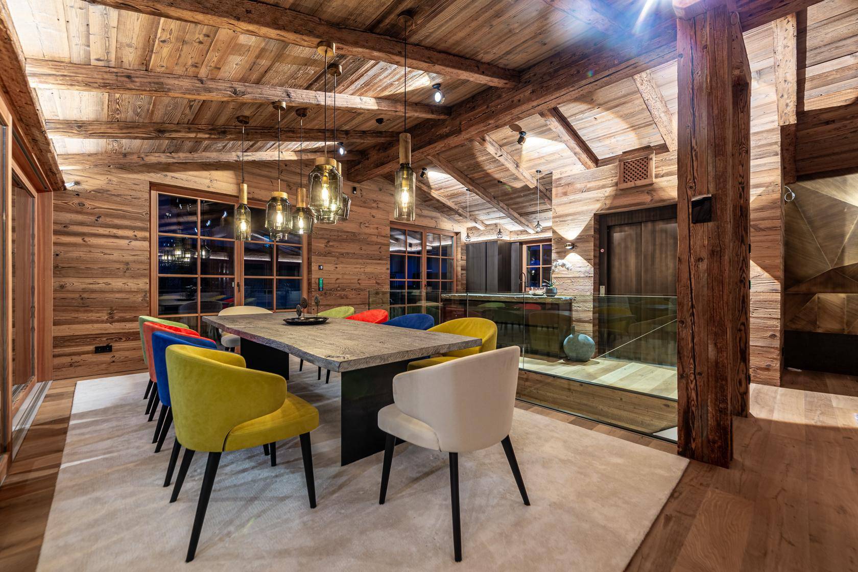 Luxuriöser Essbereich in einem Chalet mit Holzbalken, Holzwänden und farbigen Stühlen.