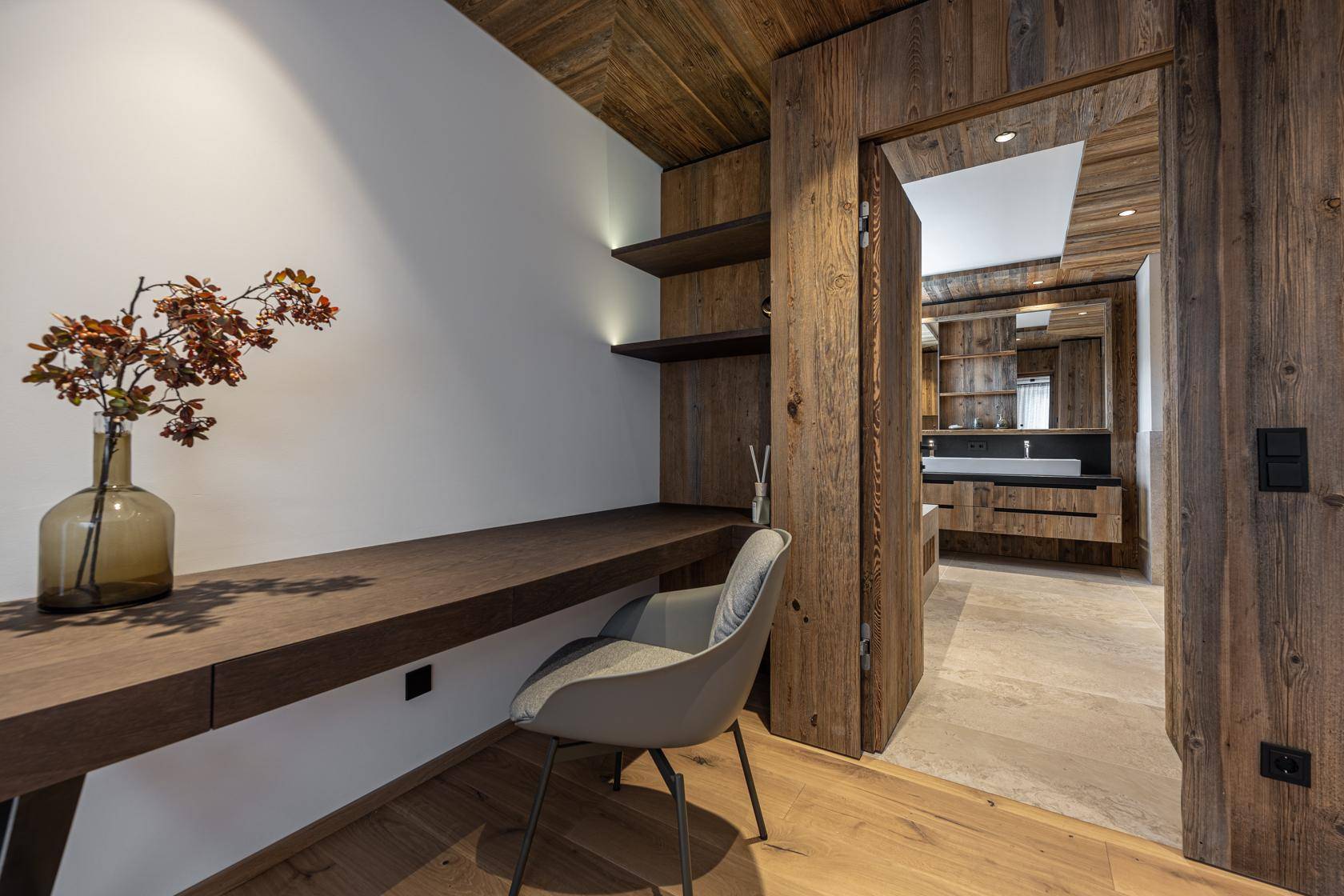Kleiner Arbeitsbereich mit Holzschreibtisch und Blick in ein angrenzendes Badezimmer.