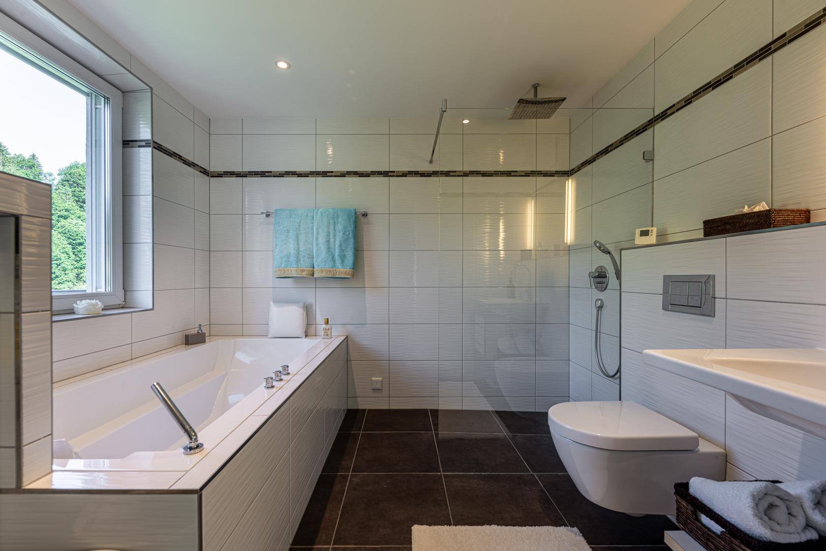 Modernes Badezimmer mit Badewanne, Regendusche, WC und Fenster.
