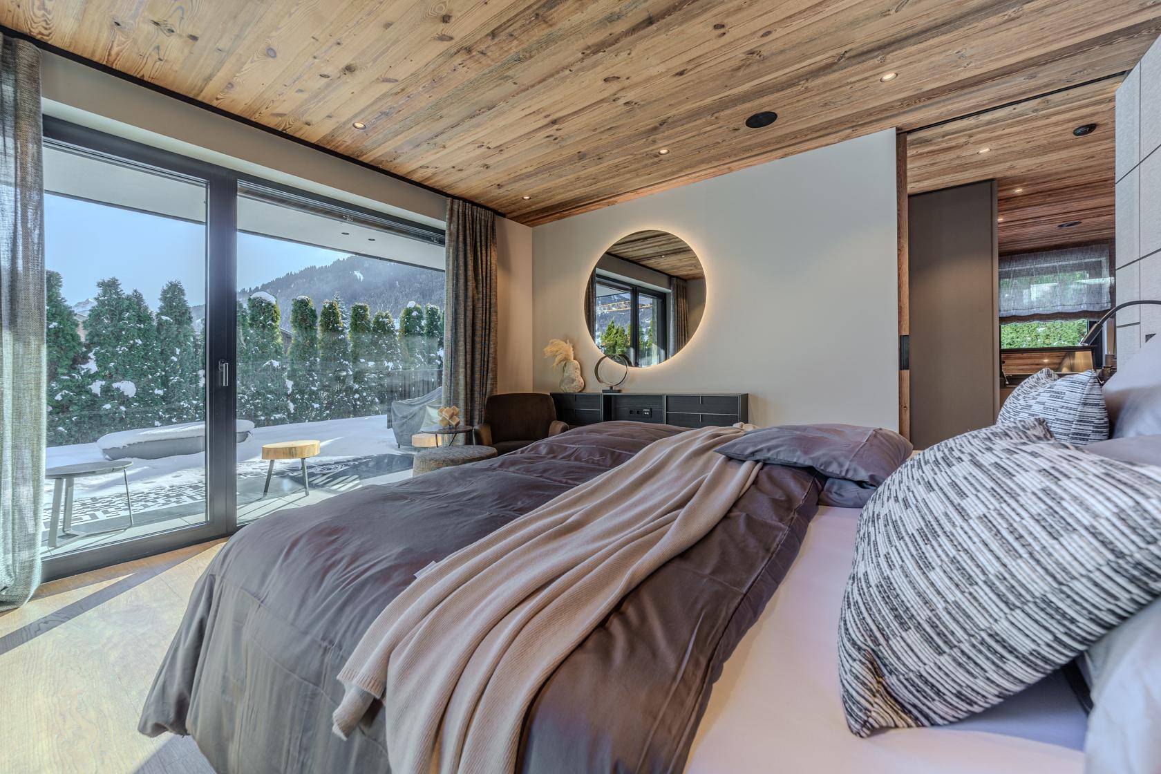 Helles Schlafzimmer mit Holzbalkendecke, Zugang zum Balkon und Blick auf die verschneite Berglandschaft.