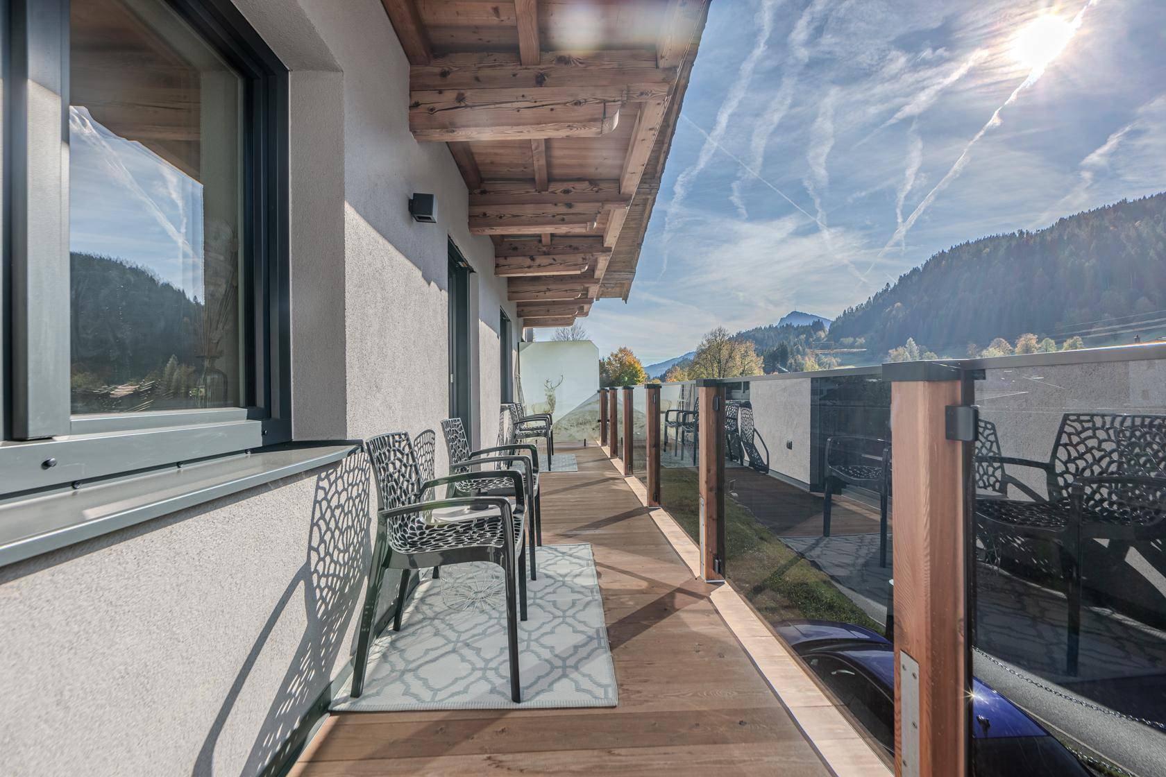 Langer Balkon mit Sitzgelegenheiten, Holzboden und Panoramablick auf die Berge.