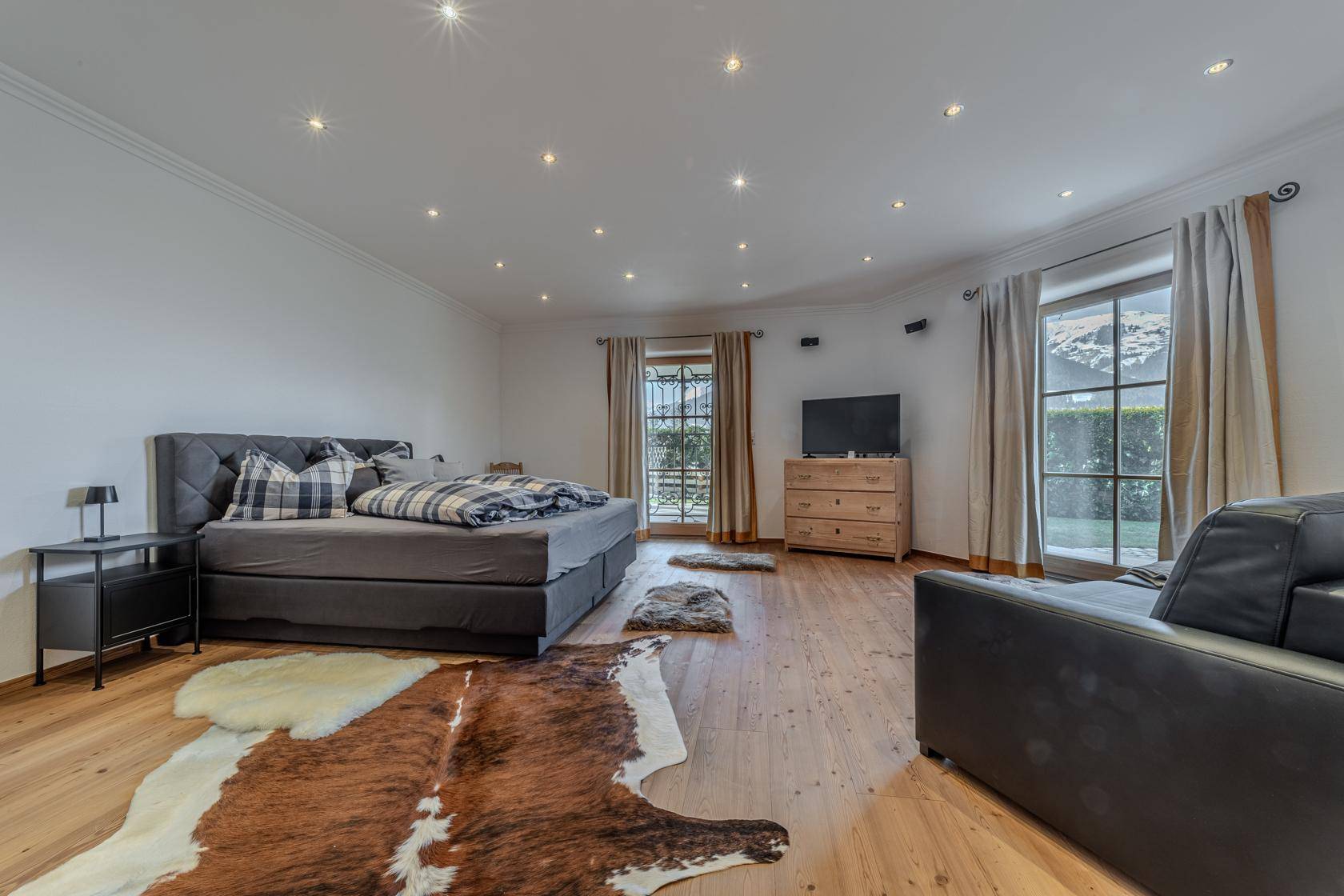 Geräumiges Schlafzimmer mit Doppelbett, Holzboden und zwei Fenstern für viel Tageslicht.