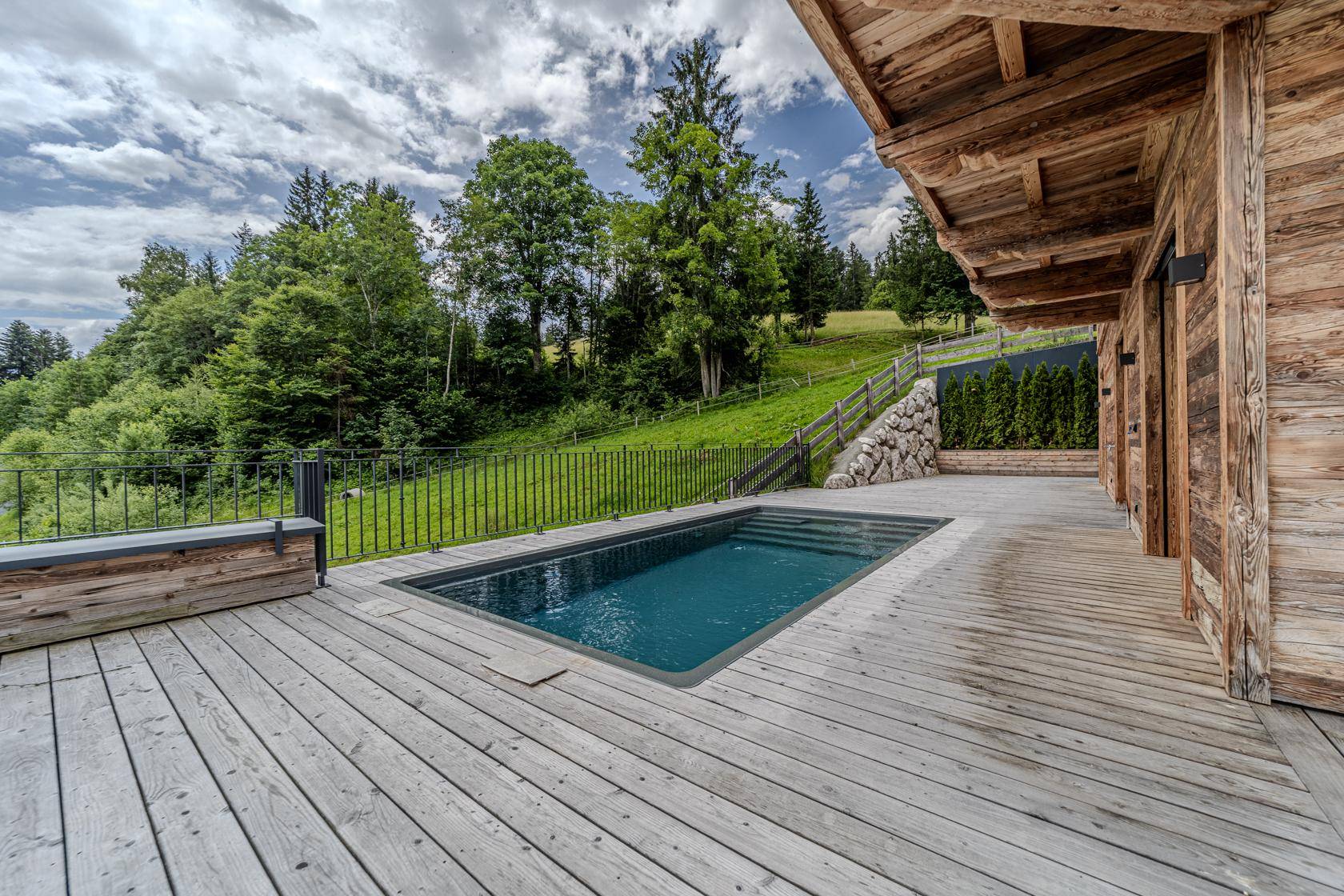 Holzterrasse mit integriertem Pool und Blick auf die umliegende grüne Landschaft.