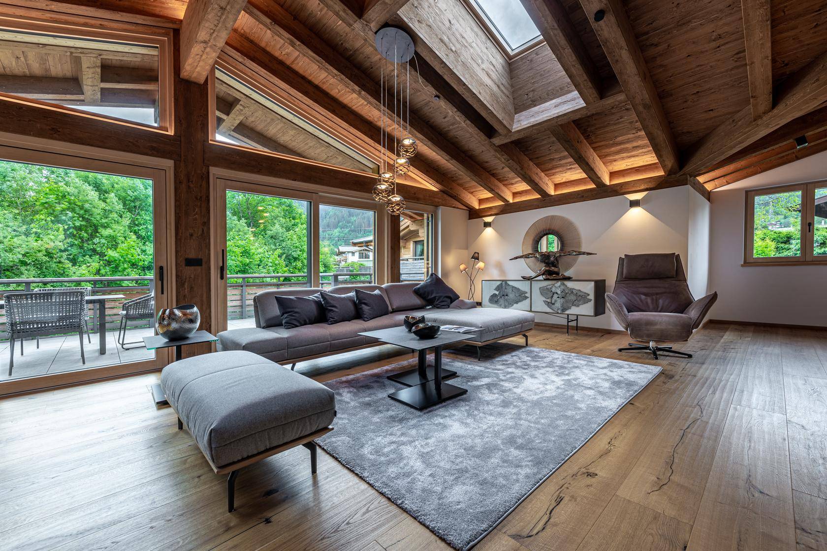 Gemütliches Wohnzimmer mit großem Sofa, Holzbalkendecke und Blick ins Grüne.