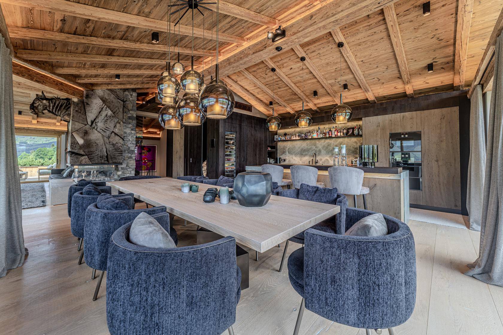 Luxuriöser Essbereich mit großem Holztisch, Designerleuchten, integrierter Bar und Holzbalkendecke.
