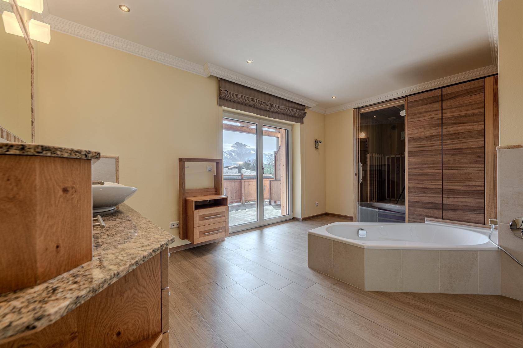 Geräumiges Badezimmer mit Eckbadewanne, Sauna und Balkonzugang mit Bergblick.