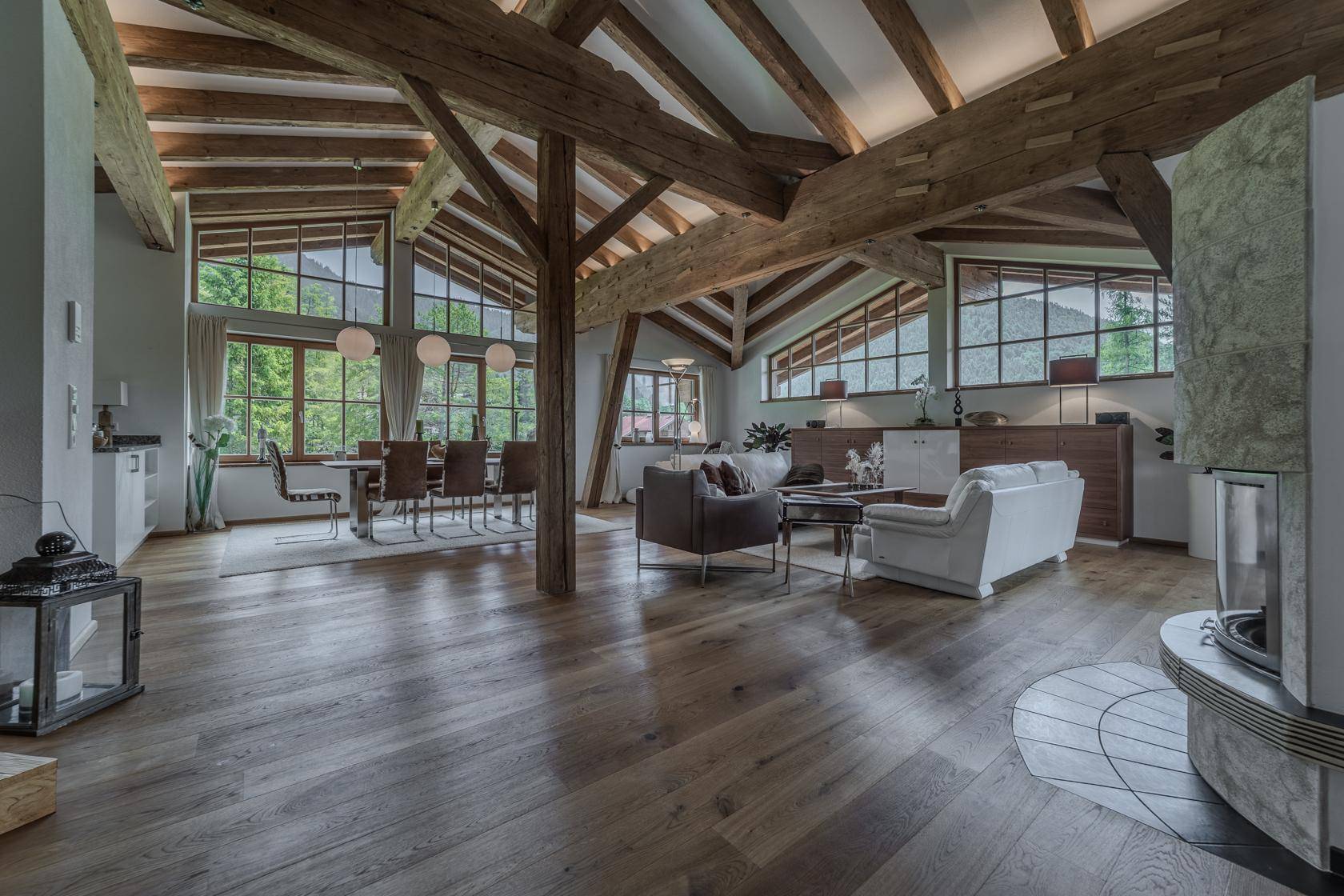 Heller Wohn-Essbereich mit Holzbalken, Kamin und großen Fenstern mit Panoramablick.