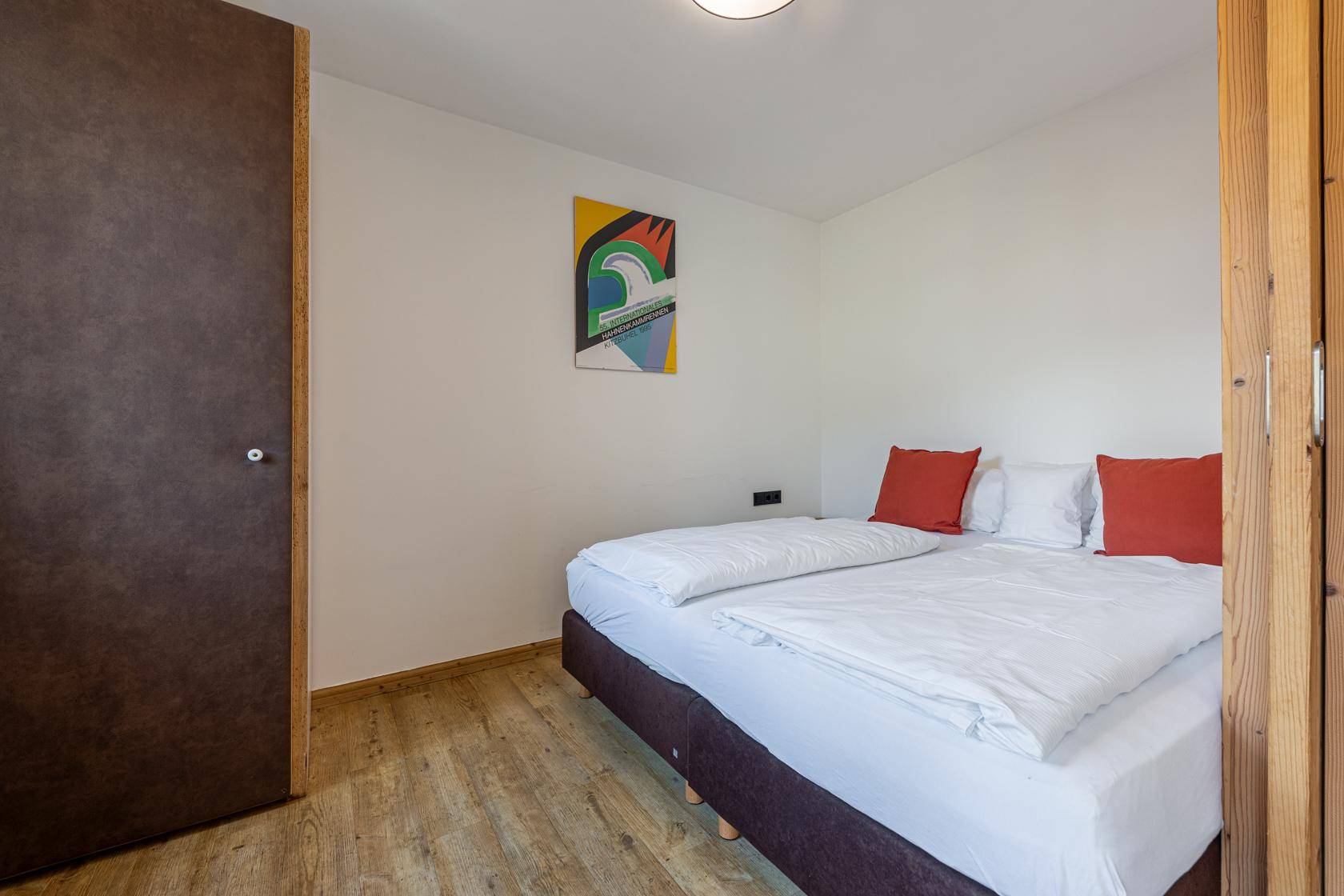 Helles Schlafzimmer mit Doppelbett, schlichtem Design und einem farbenfrohen Kunstwerk an der Wand.