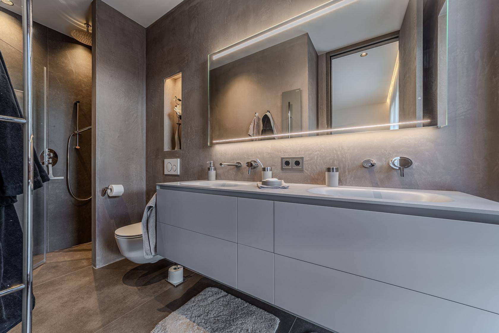 Elegantes Badezimmer mit Doppelwaschbecken, Wand-WC und großer Dusche.