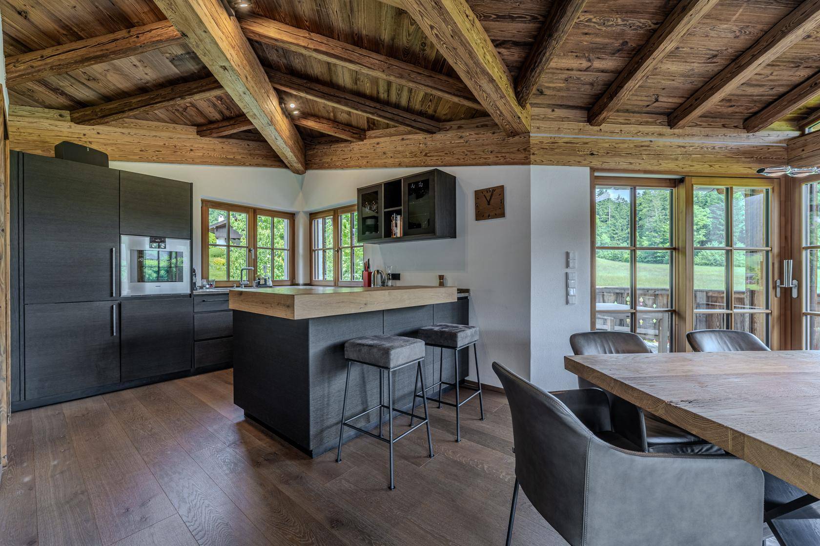 Moderne Küche mit dunklen Schränken, Holztheke und Essbereich mit Balkonzugang.