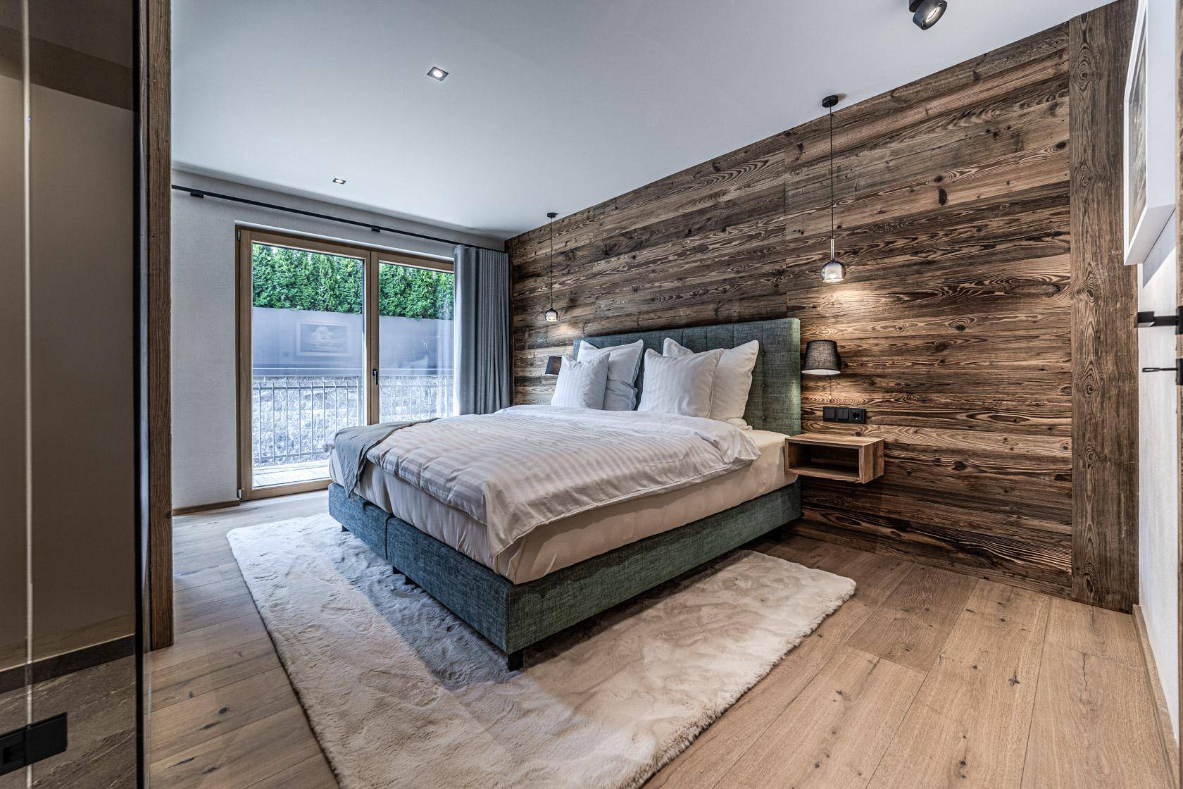 Helles Schlafzimmer mit Holzwand, Holzboden und direktem Zugang zum Balkon.