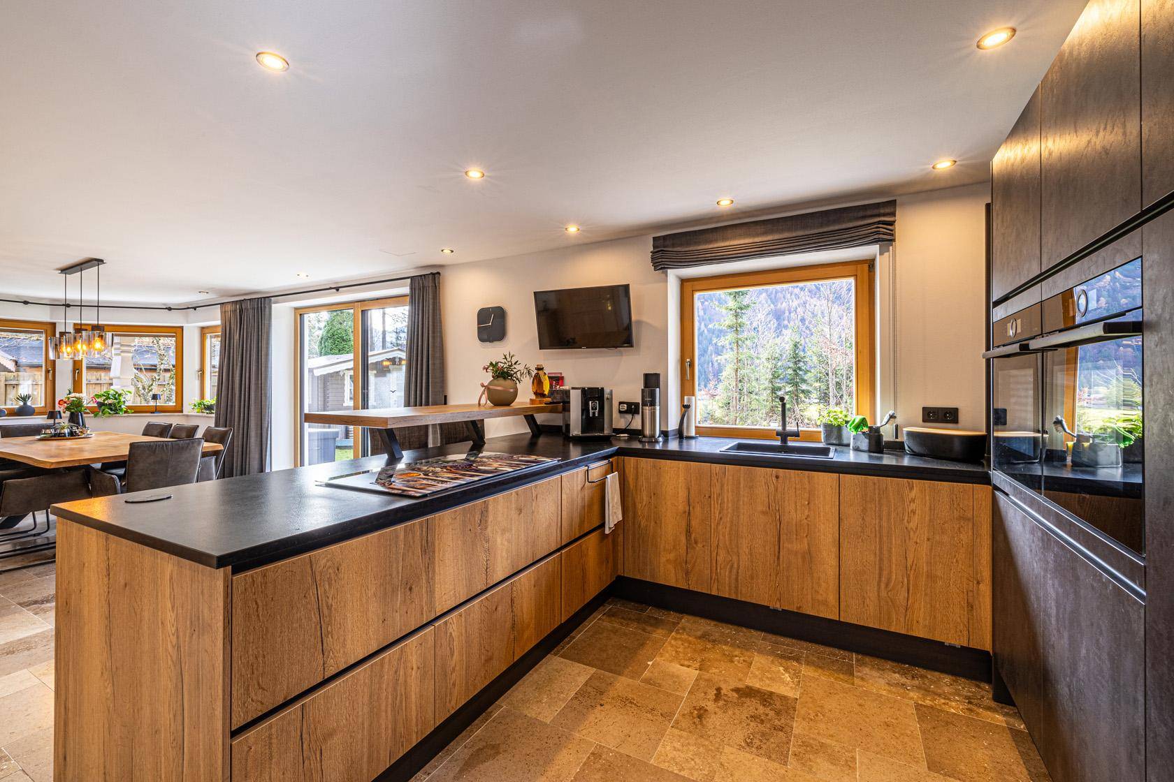 Moderne offene Küche mit Holzfronten, dunkler Arbeitsplatte und Bergblick durch das Fenster.