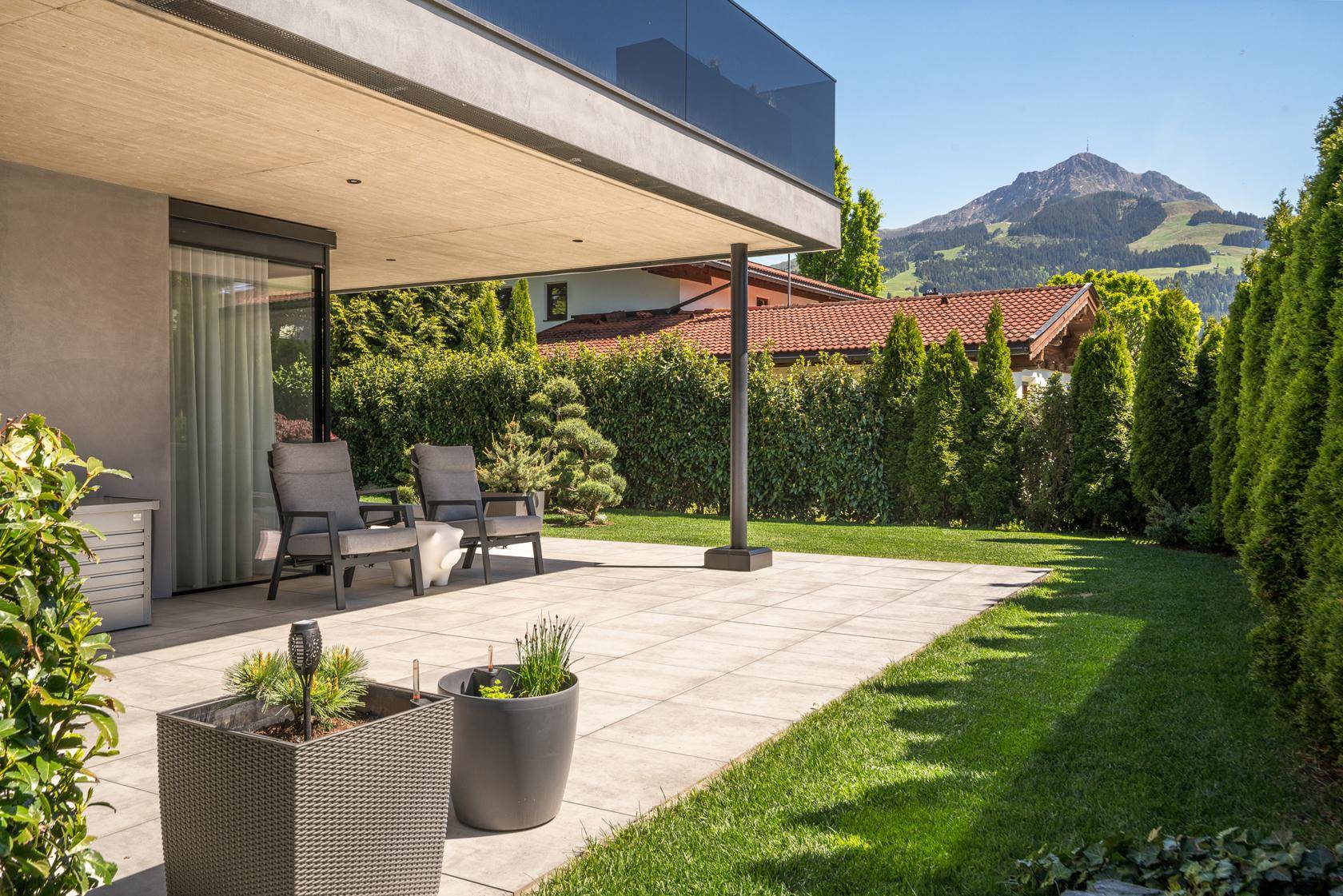 Sonnige Terrasse mit Sitzgelegenheiten, Pflanzen und Blick auf die umliegende Berglandschaft.