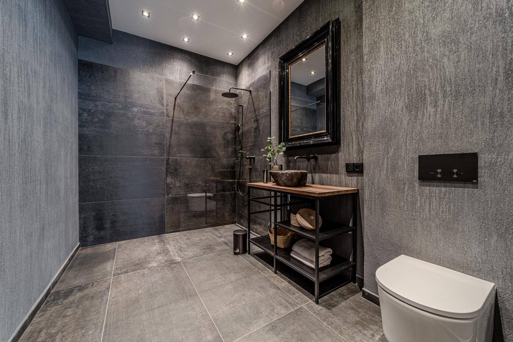 Modernes Badezimmer mit dunklen Fliesen, begehbarer Dusche und stilvollem Waschtisch.