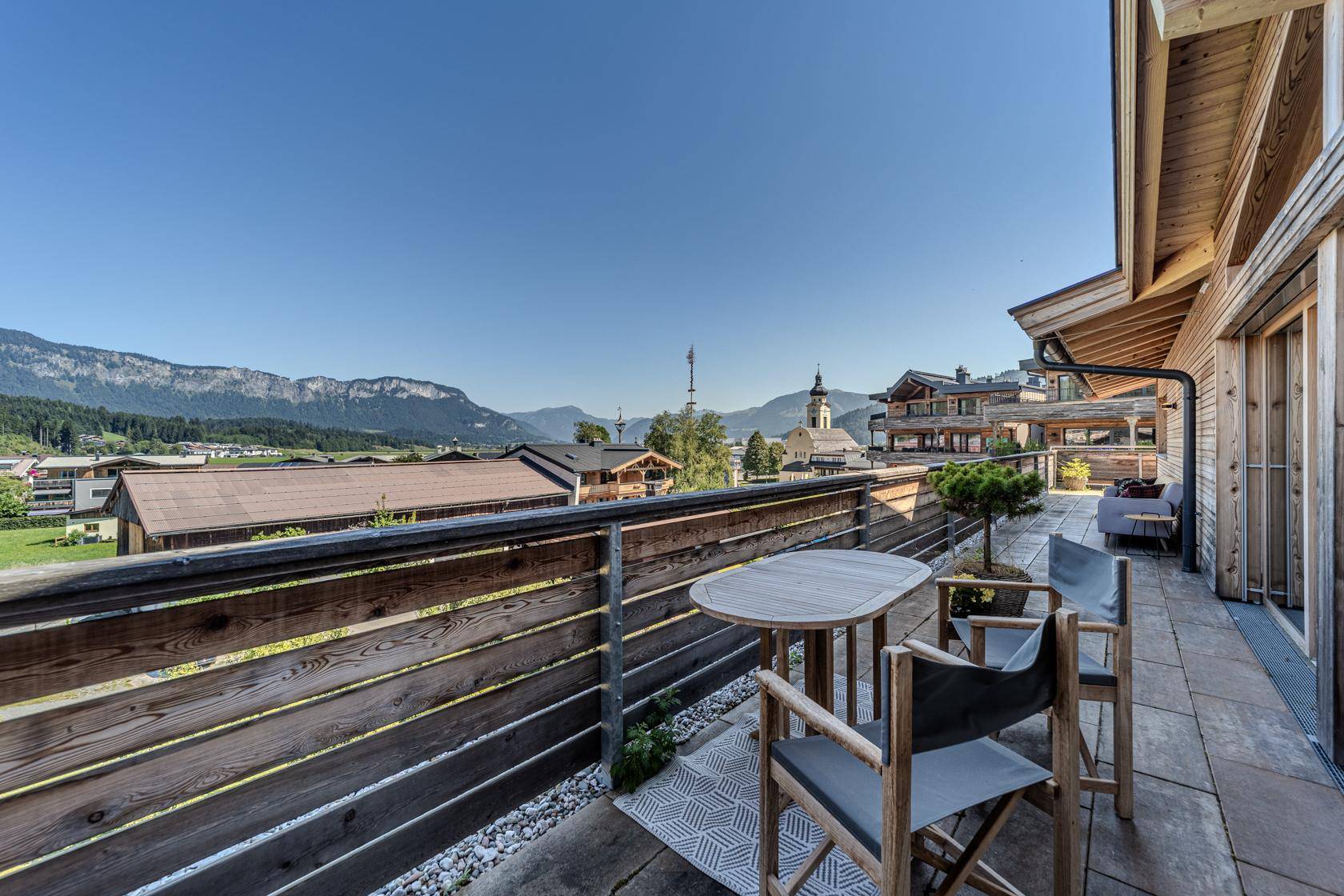 Lange Terrasse mit Holzzaun, Sitzbereich und weitem Blick über die Landschaft.