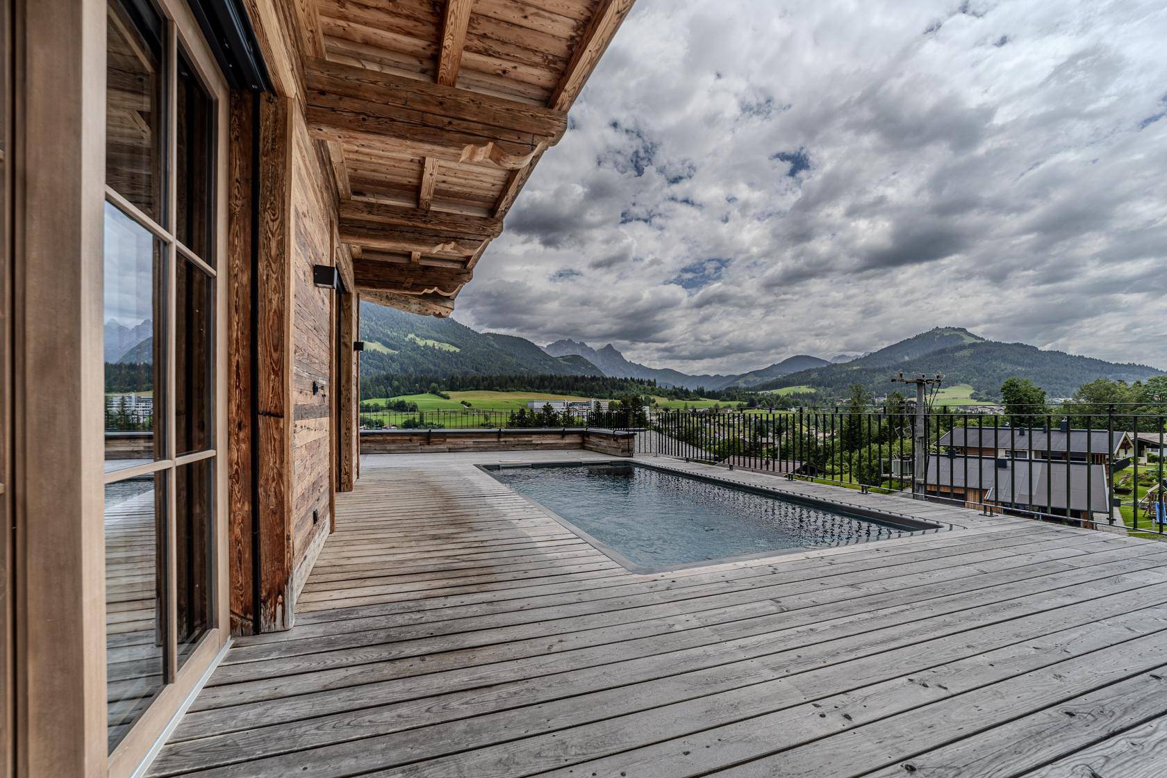 Große Holzterrasse mit Pool und weitem Panoramablick auf die Berge und das Tal.