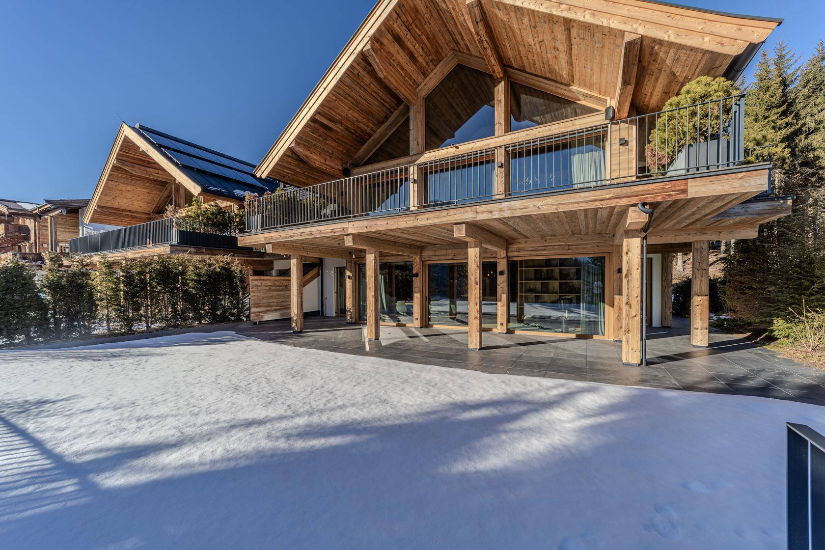 Moderne Holzarchitektur mit großer Terrasse und Blick auf die verschneite Landschaft.