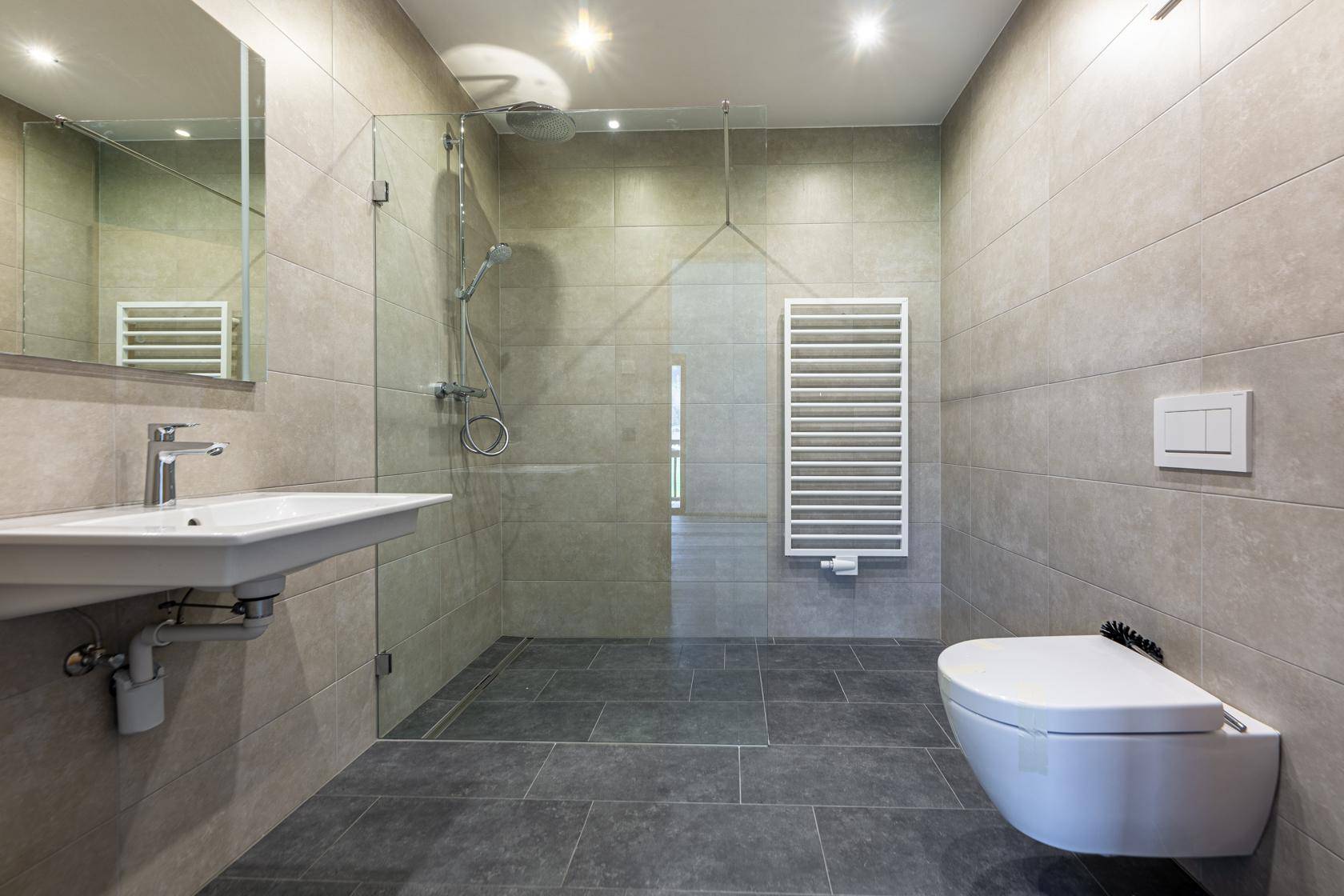 Modernes Badezimmer mit grauen Fliesen, einer begehbaren Dusche und einem wandhängenden WC.