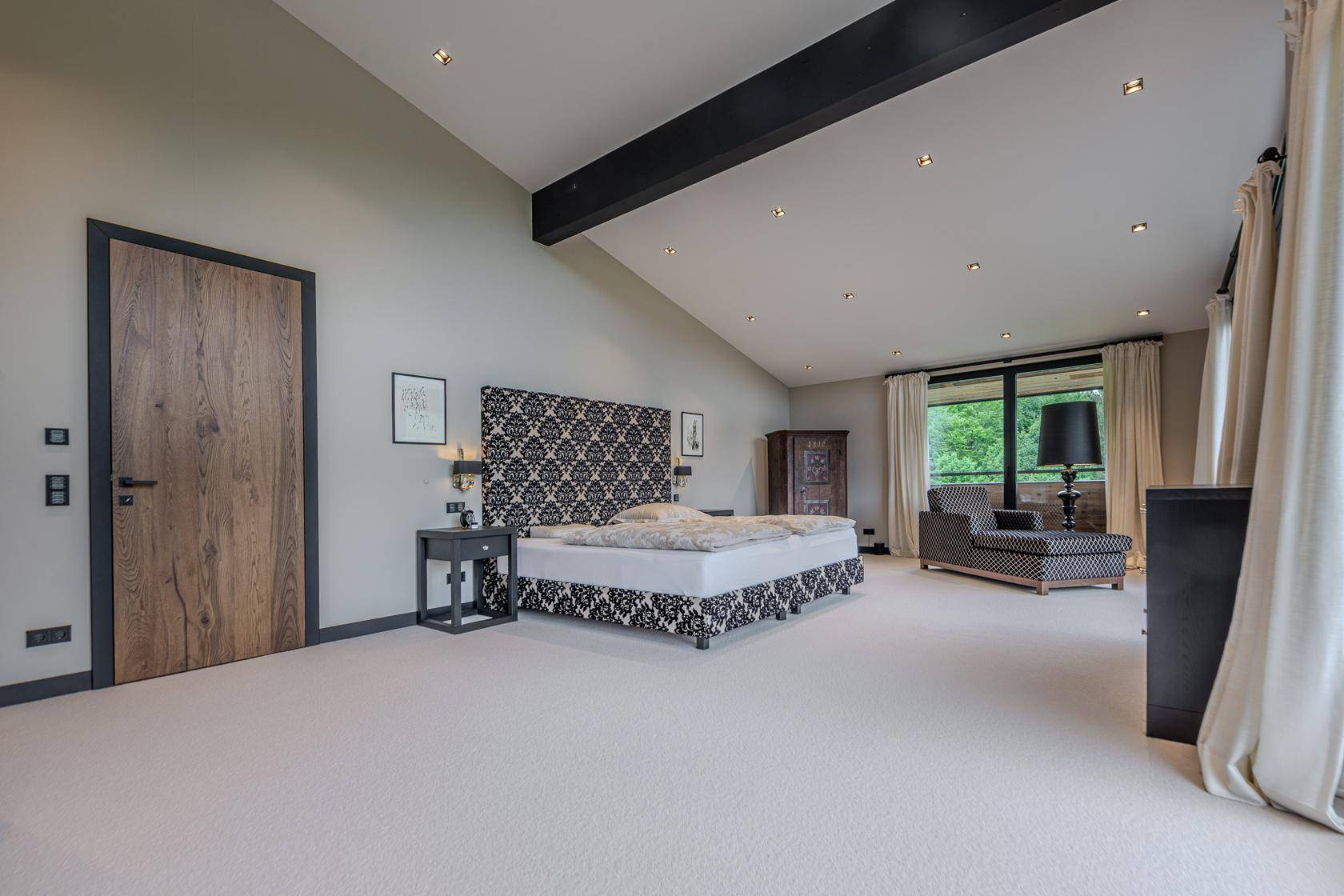 Großes Schlafzimmer mit Teppichboden, hohen Decken und Blick auf die umliegende Natur.