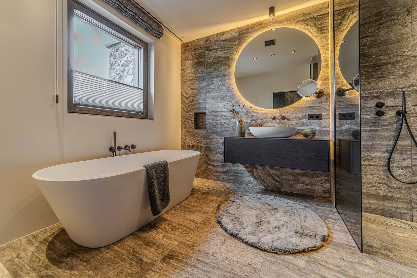 Luxuriöses Badezimmer mit freistehender Badewanne, großer Dusche und modernem Waschtisch mit beleuchtetem Spiegel.