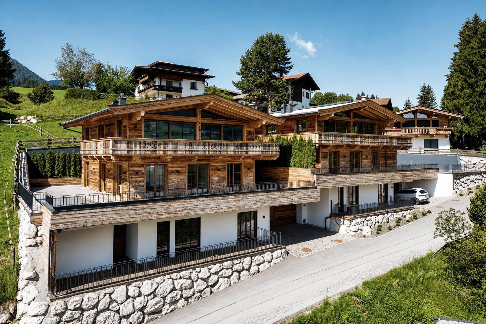 Zwei moderne Chalets mit Holzfassade und Balkonen in alpiner Hanglage.