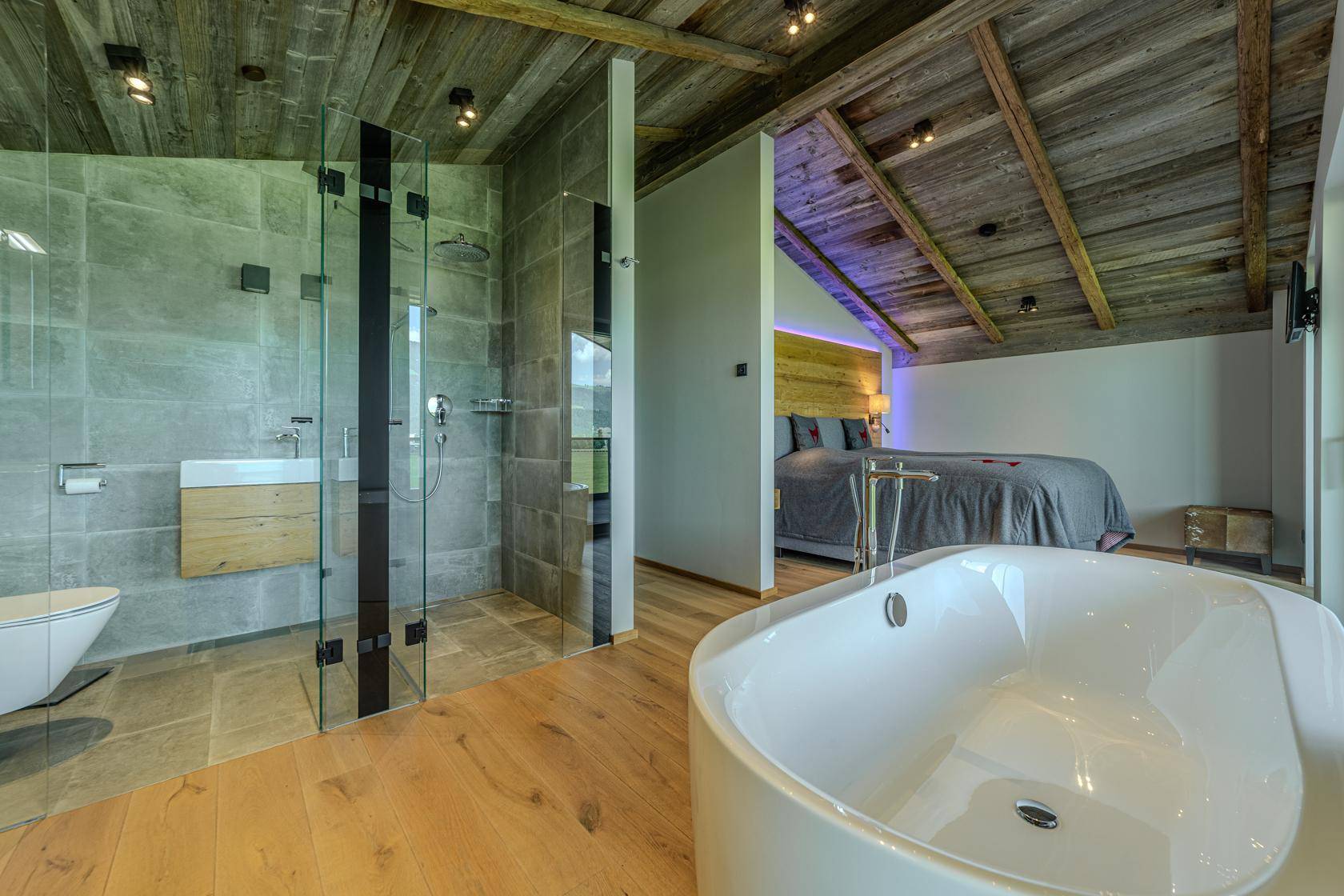Modernes Badezimmer mit begehbarer Dusche, WC und freistehender Badewanne im Schlafzimmerbereich.
