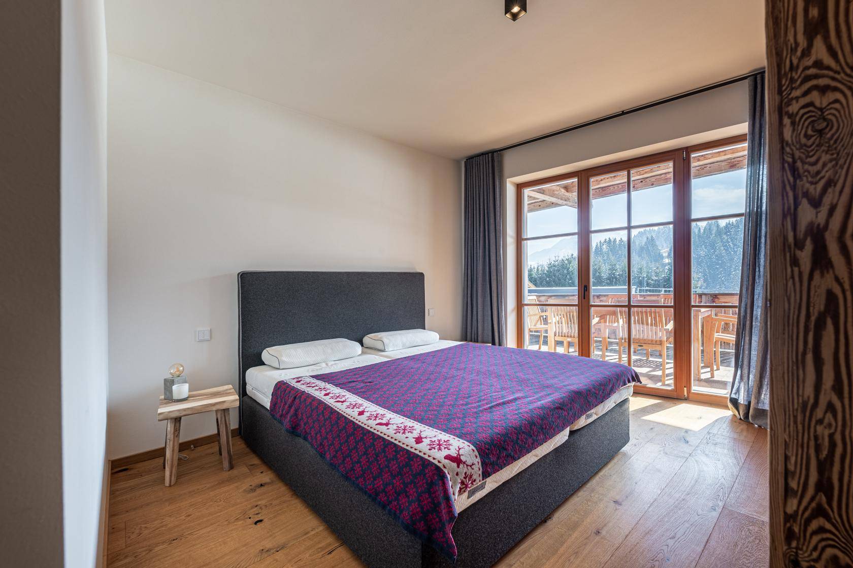 Gemütliches Schlafzimmer mit Doppelbett, Holzboden und direktem Balkonzugang.