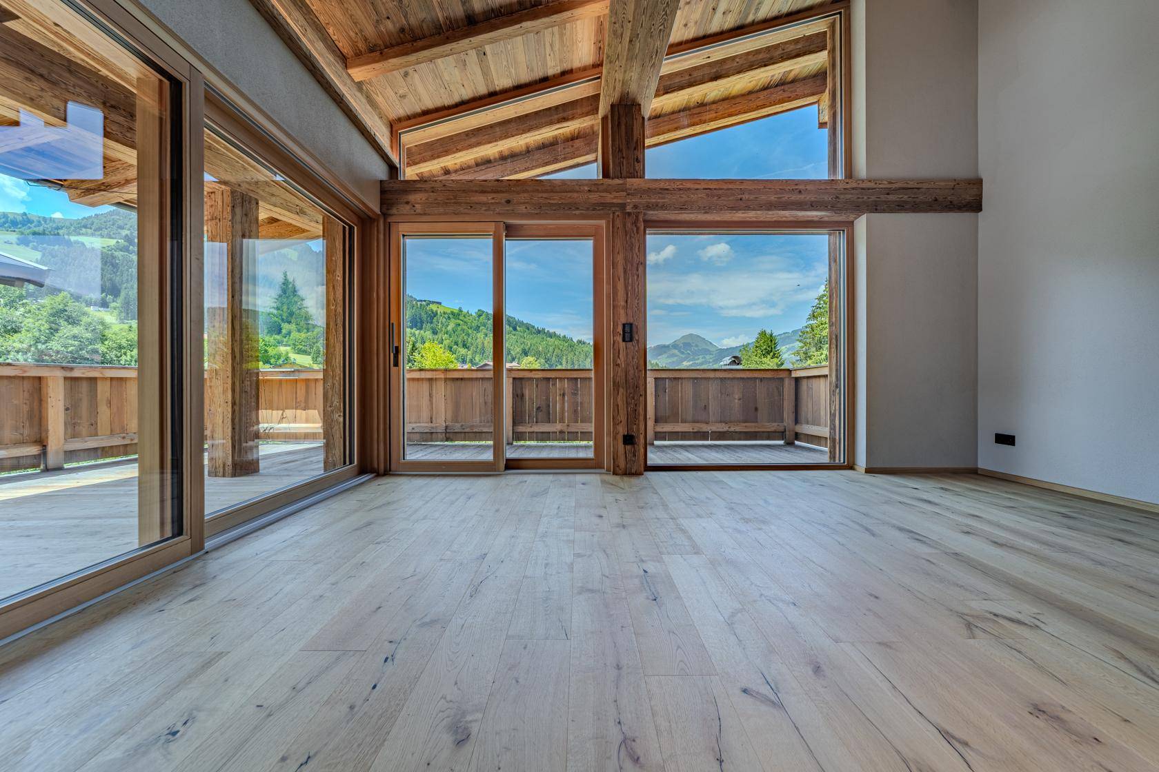 Heller Wohnraum mit Holzbalken, großen Fensterfronten und Panoramablick auf die Berge.